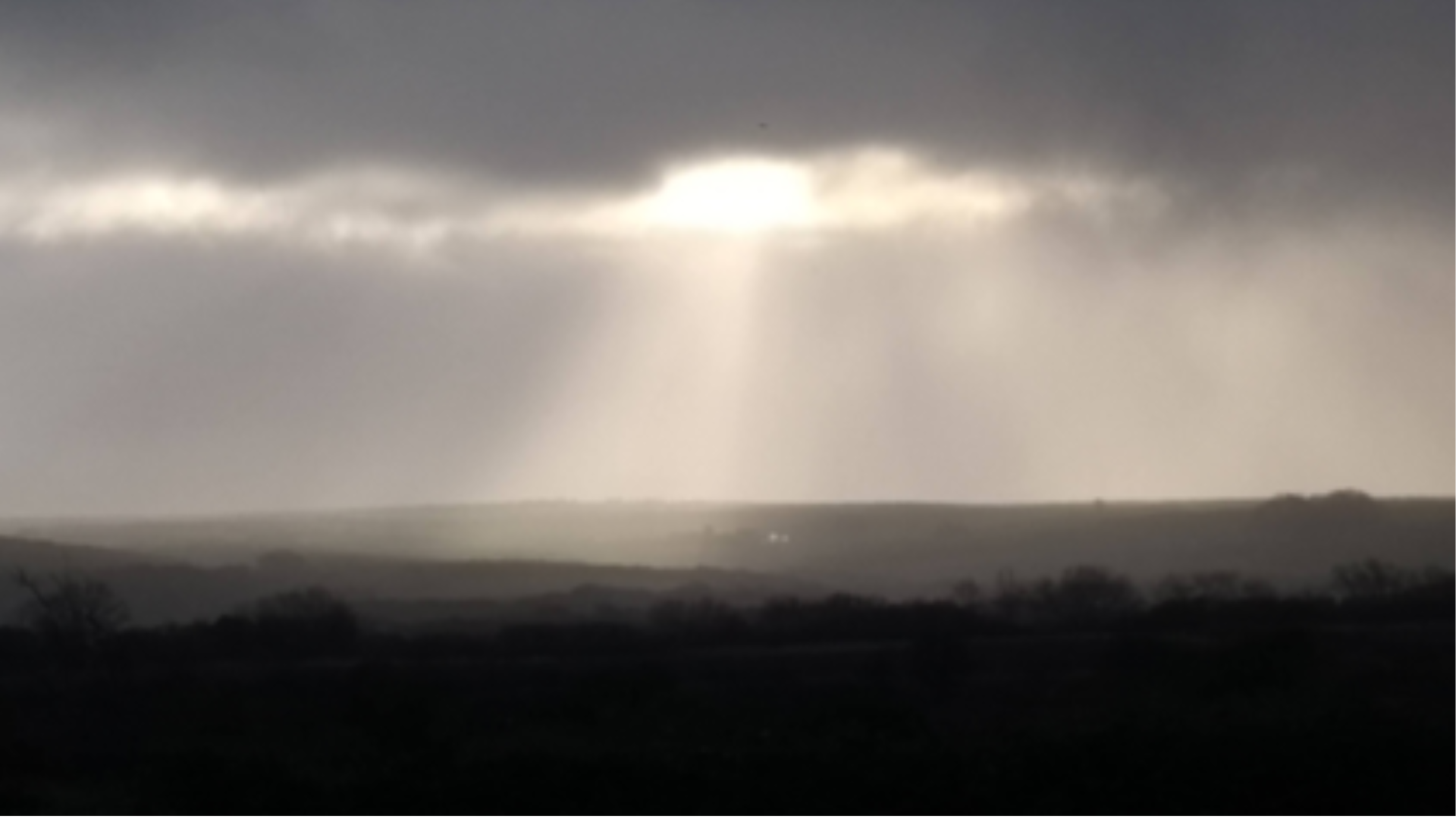 Beams of sunlight breaking through grey clouds onto the landscape